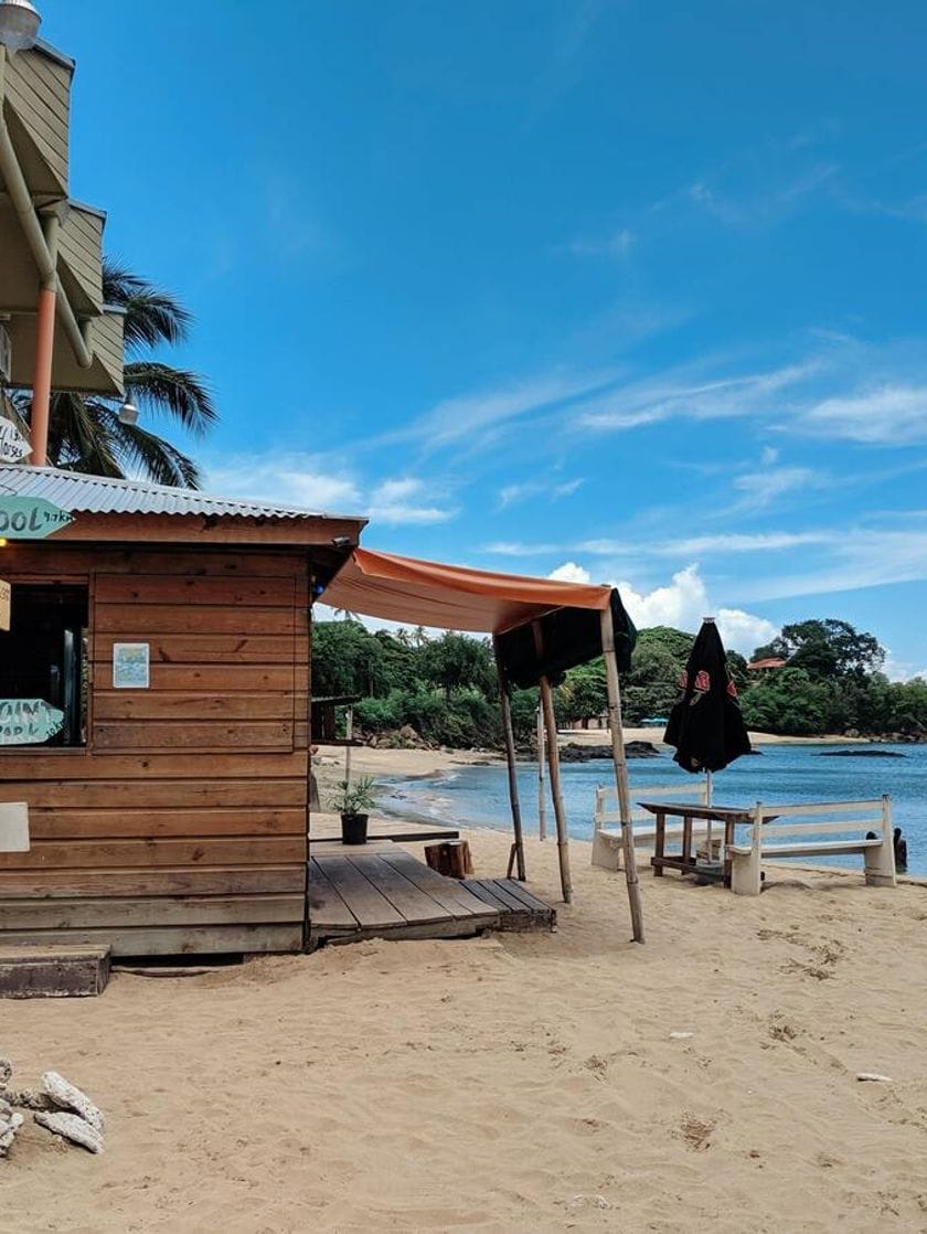 A wooden hut and a table with benches on a white sandy beach.