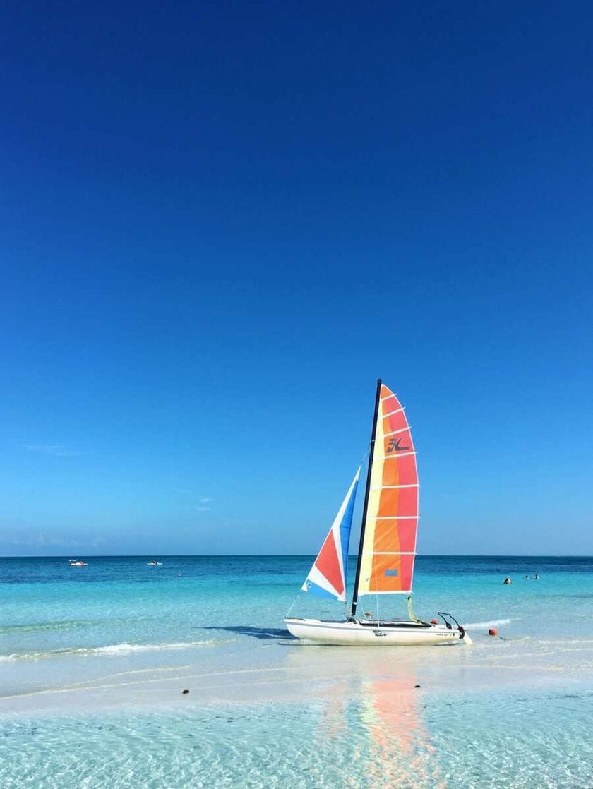 A red and white sailbot moving through the clear azure waters under a deep blue sky.