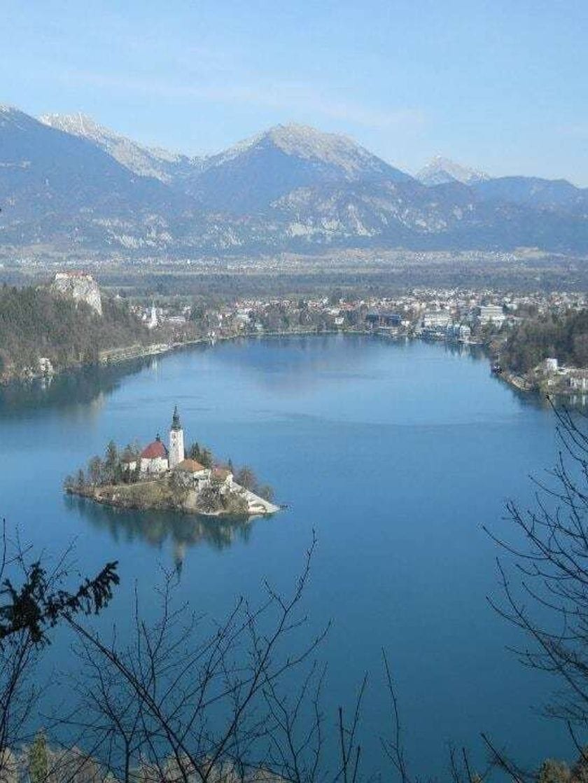 A white church on a small island in the middle of a lake with mountains in the distance. 