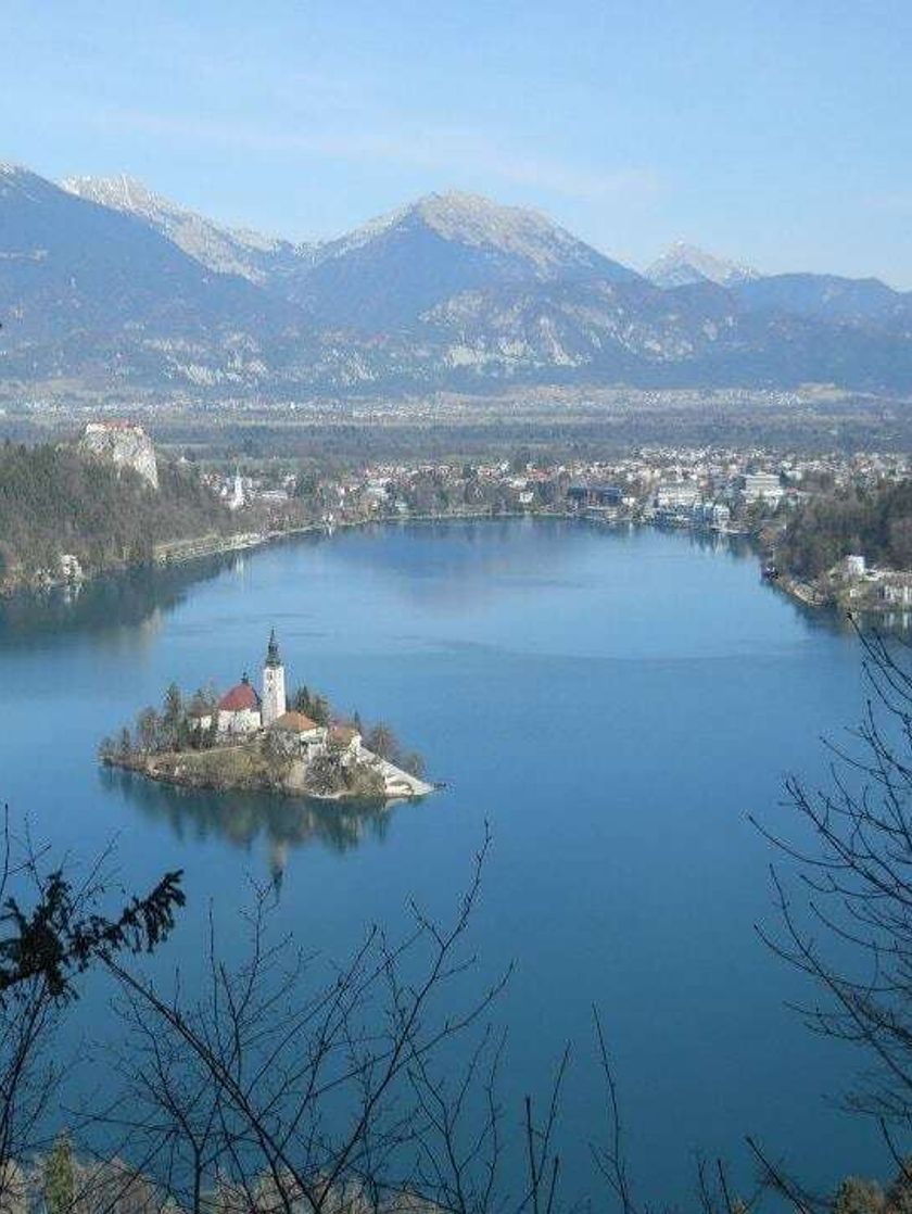 A white church on a small island in the middle of a lake with mountains in the distance. 
