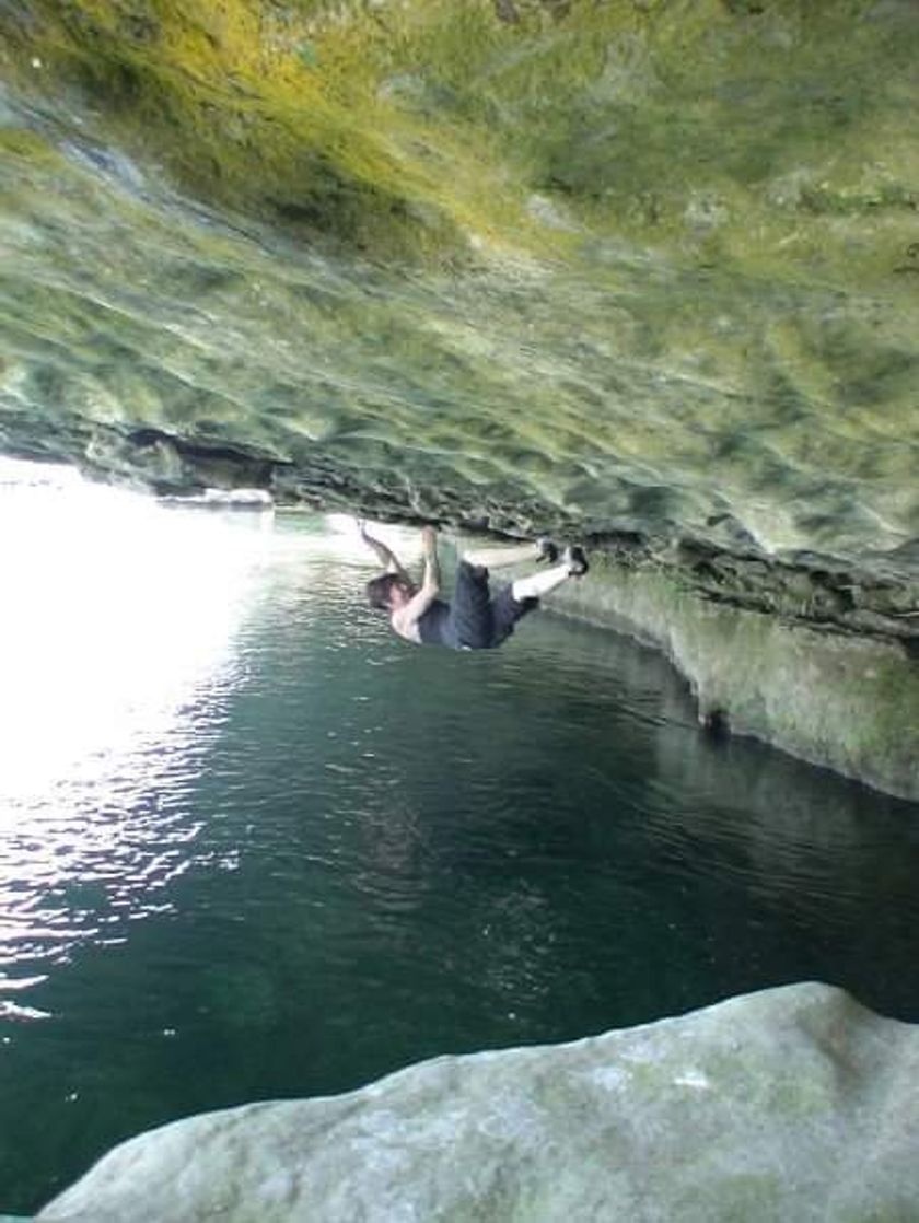 A woman grips a rock face that spans horizontally over a body of water.