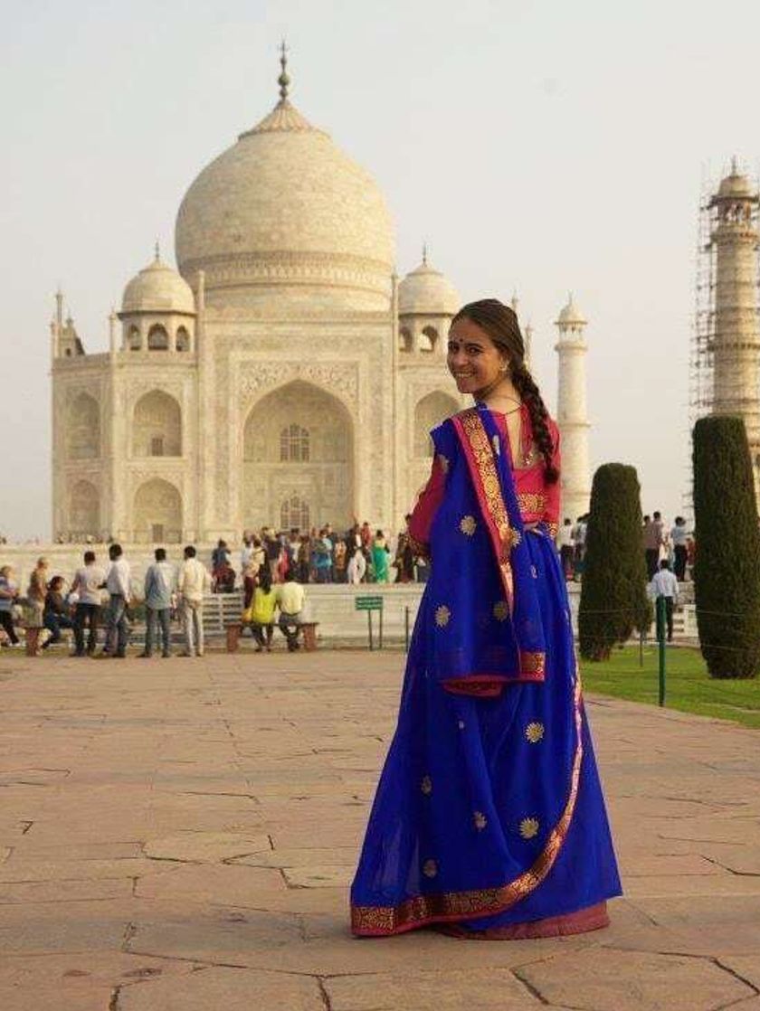 A woman wearing a vibrant blue and pink sari, standing in front of the at the Taj Mahal.