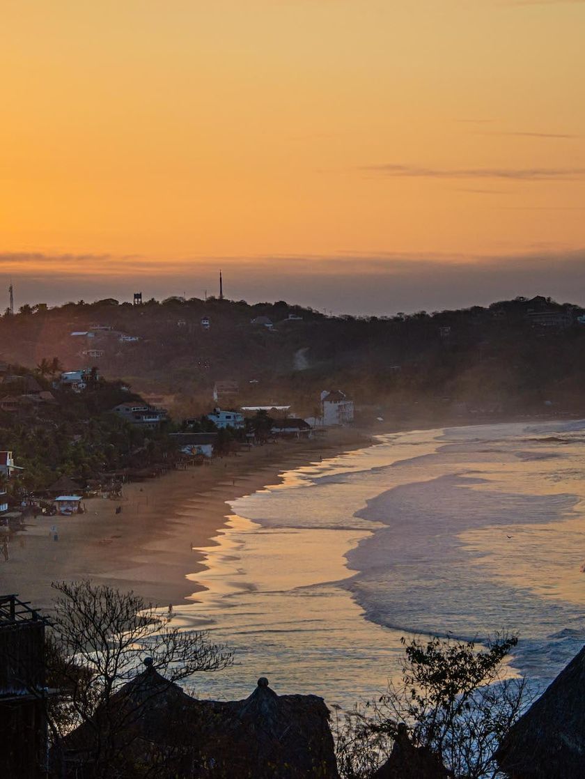 A small town nestled in hilsides along an ocean coastline at sunset.