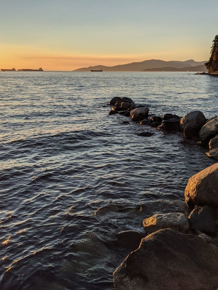 Sunset at English Bay with waves rolling up against the rocks.